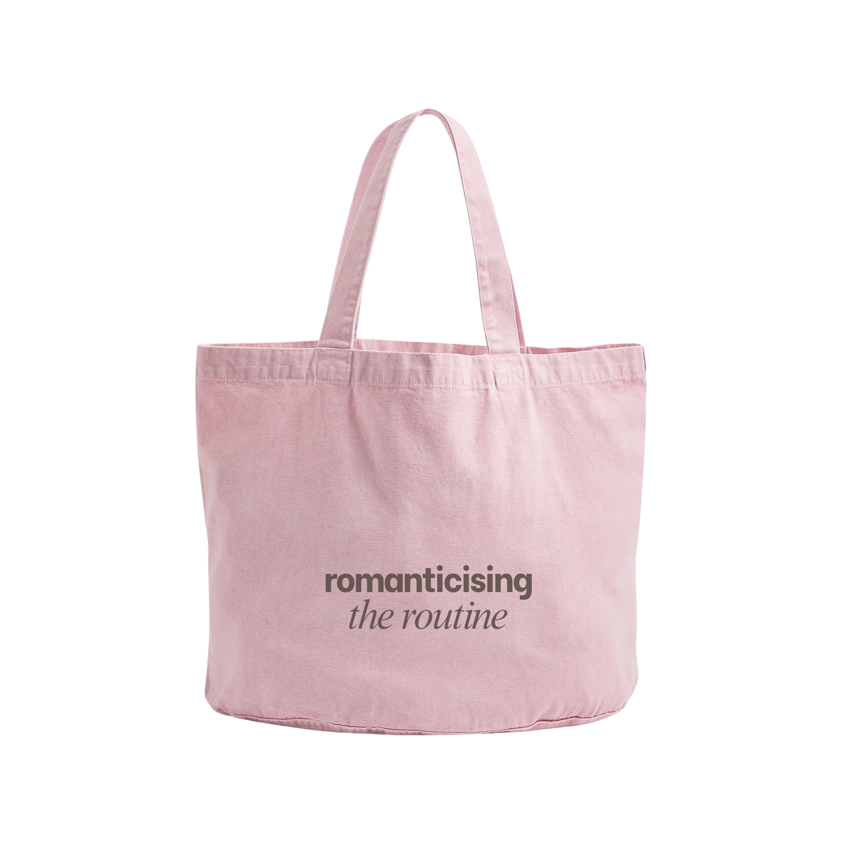 A light pink canvas tote bag with two shoulder straps, featuring the printed text 'romanticising the routine' in dark gray on the front, set against a plain white background.