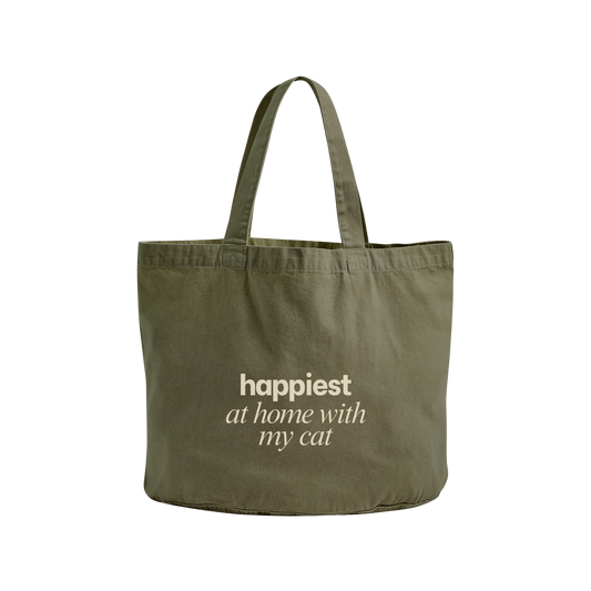 An olive green canvas tote bag with the phrase 'happiest at home with my cat' printed in cream-colored text on the front, set against a plain white background.