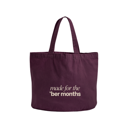 A dark purple canvas tote bag with two shoulder straps, featuring the text 'made for the 'ber months' printed in a light beige font on the front, set against a plain white background.